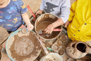 Children playing with mud in bowls with utensils.