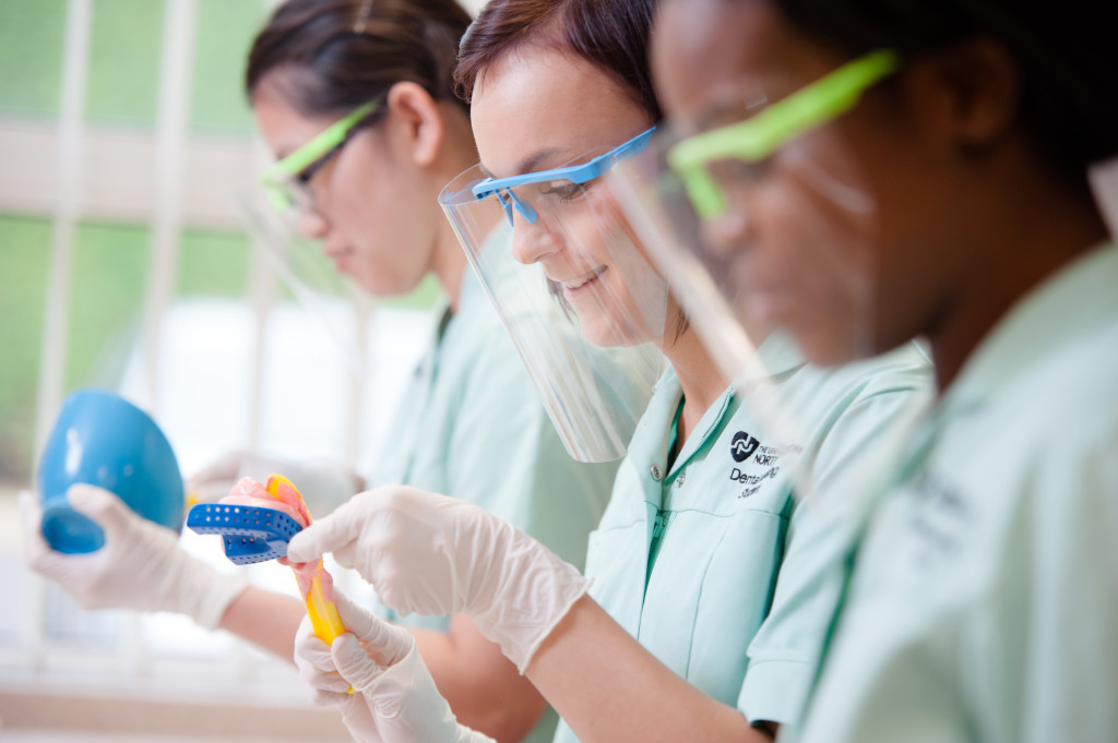 Dental nursing students during a practical, wearing a face shield while working with dental instruments.
