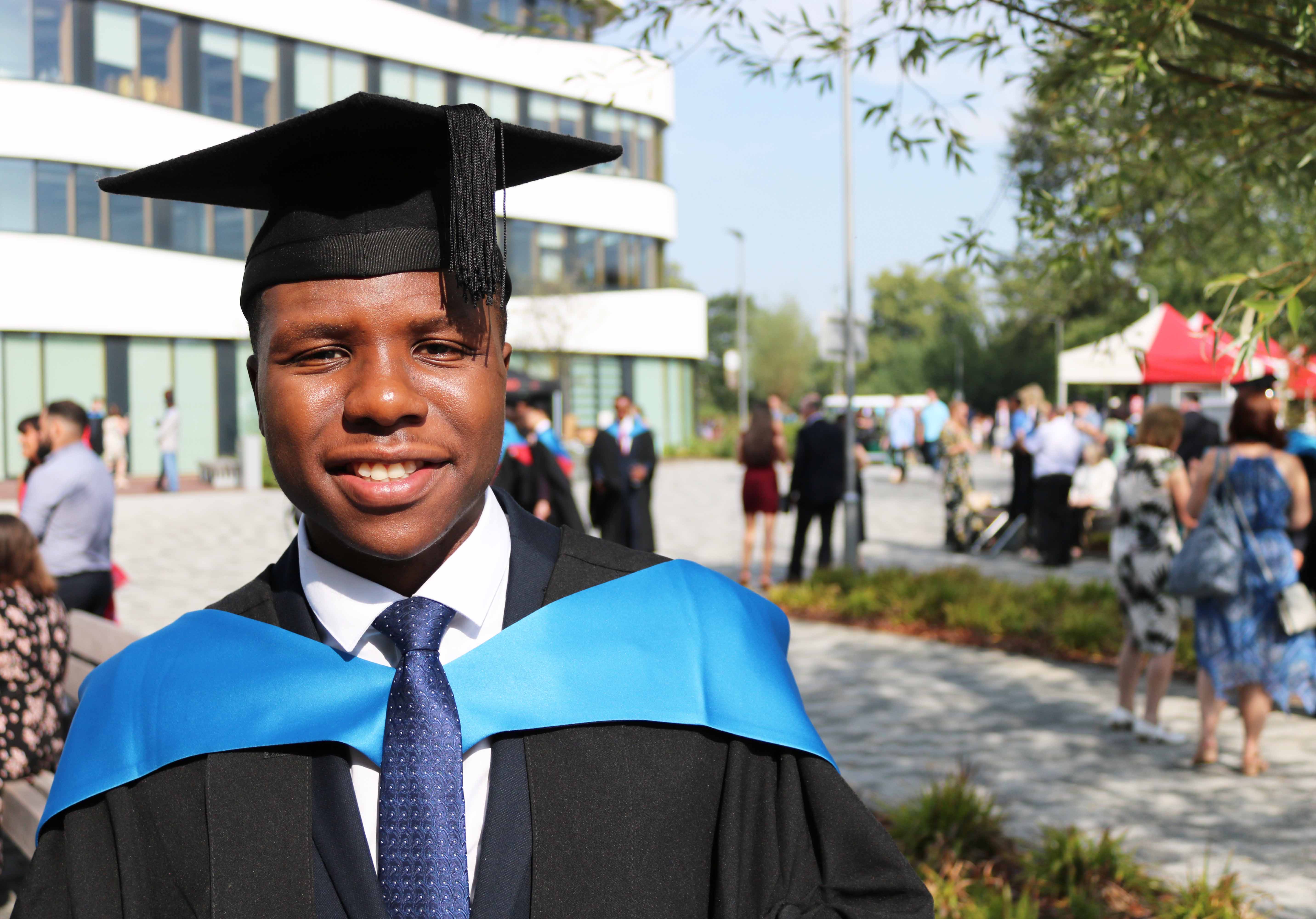 Pic of Michael Gukas in cap and gown outside the Learning Hub on Waterside campus