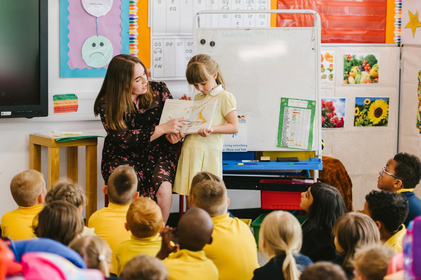 A teacher with a child holding a book in front of a class