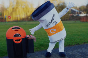 Cuppy, the Up the Cup mascot next to a recycling bin
