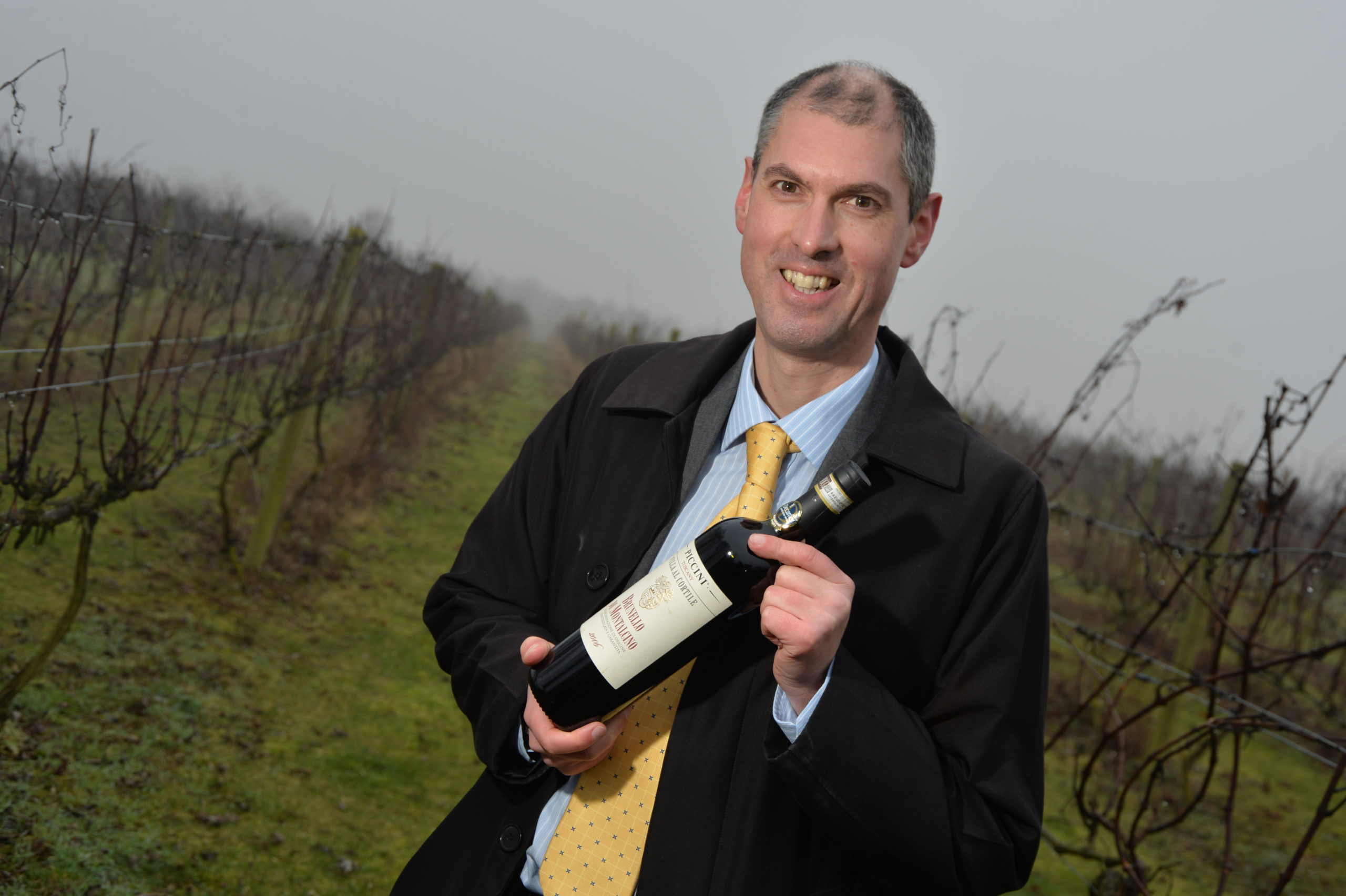 A picture of Simon Wragg, at a vinyard with a bottle of wine