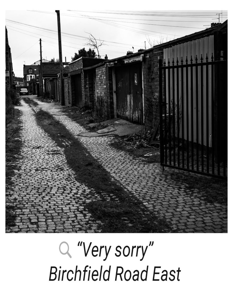 An alleyway with rubble and broken garages with a quote alongside it “very sorry”, Birchfield Road east