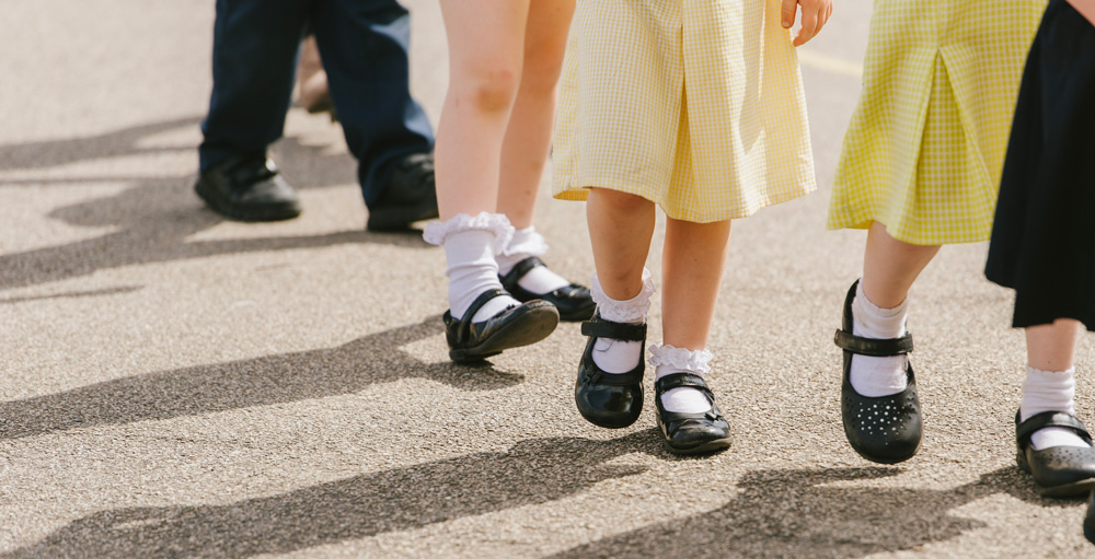 Legs and shows of school children, walking on playground. Their shadows are on the ground.
