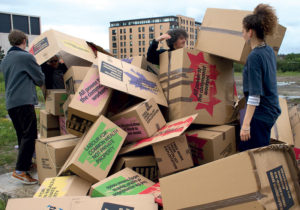 Three students with pile of cardboard boxes of various shapes and sizes in a pile.