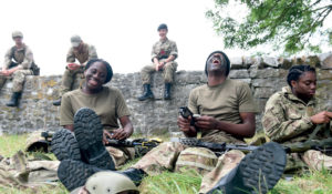Six cadets sitting on grass and on a wall. They are smiling and laughing.