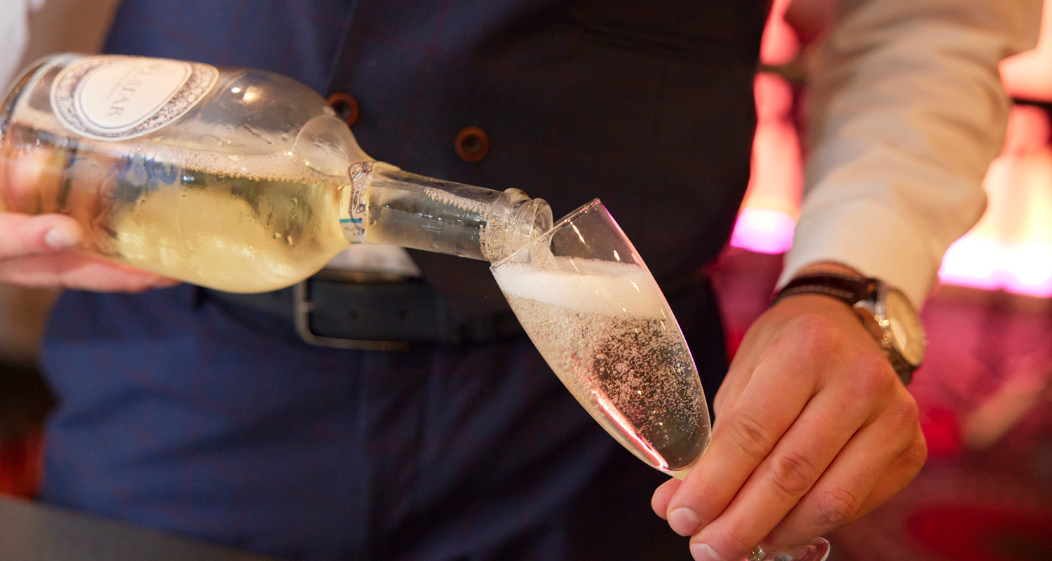 Person pouring bubbly drink into flute glass, with bubbles in the drink.