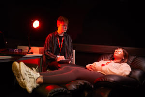 Two students using the Perception Lab. One is laying down and the other is holding a clipboard. They are in a dark room.