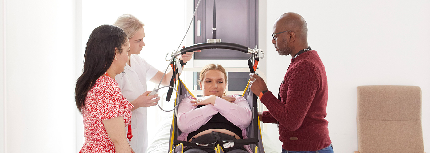 Two Occupational Therapy students and an academic, with a volunteer demonstrating the bed lift.