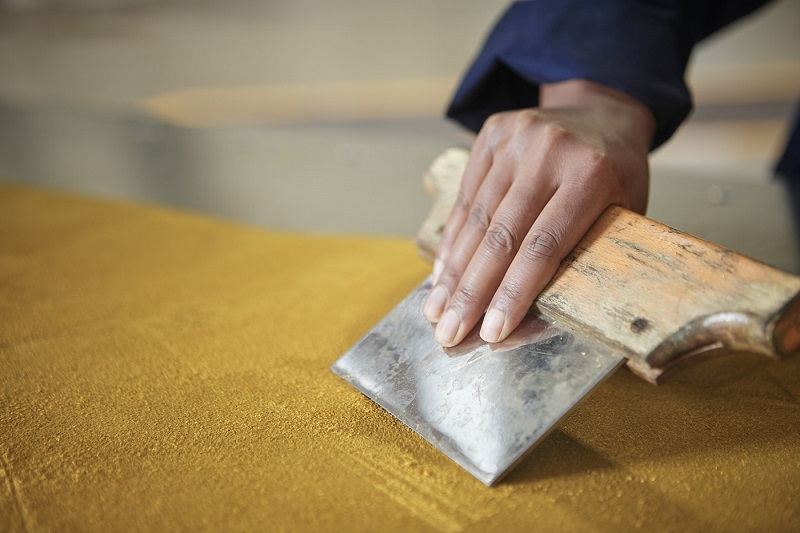 Hand using a leather-making tool on a dark yellow piece of leather