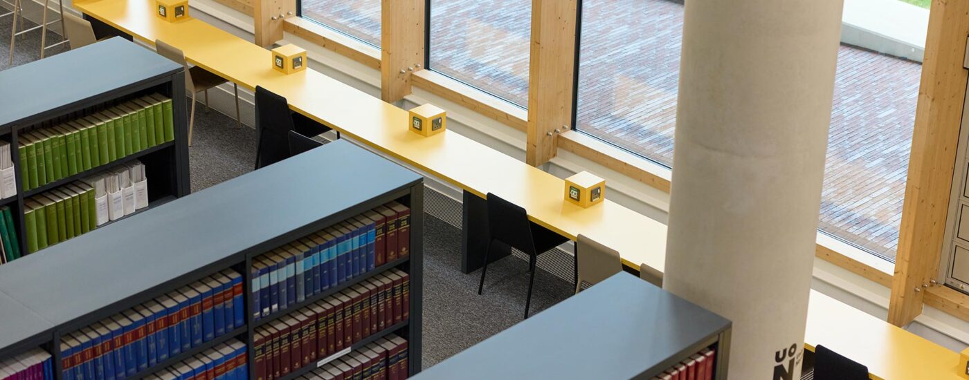 Corner of library shelves with thick, hardback law books, and a long yellow desk with plug sockets and chairs