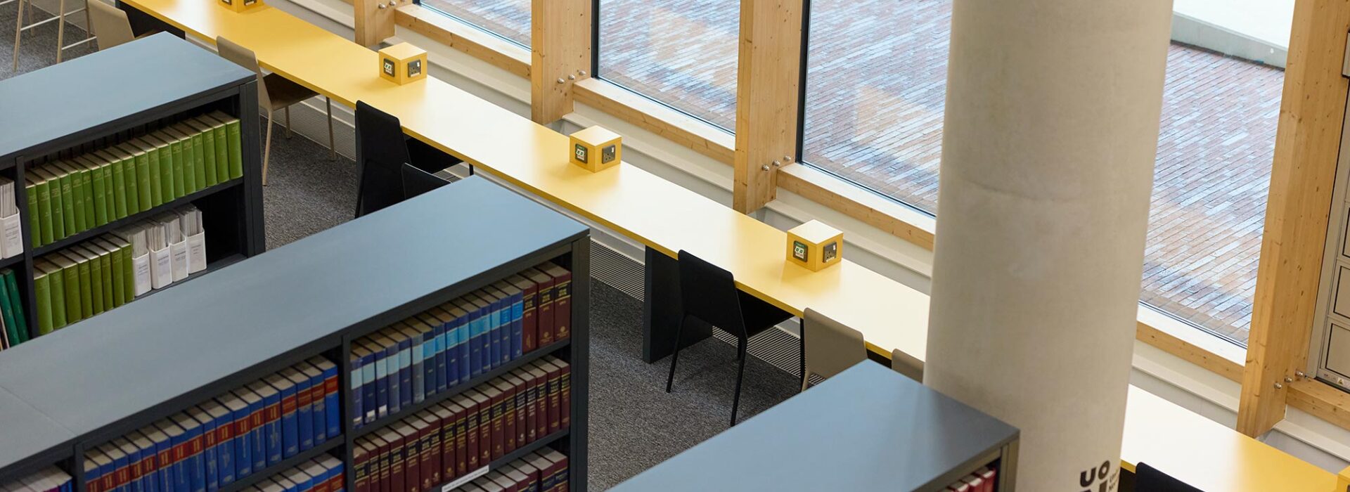 Corner of library shelves with thick, hardback law books, and a long yellow desk with plug sockets and chairs