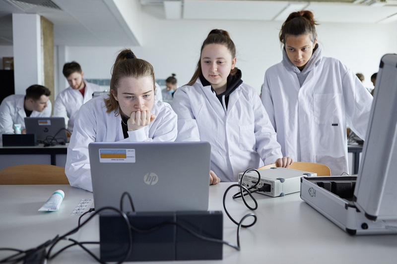 Three students checking experiment results on laptop in a Biomedical Sciences lab.