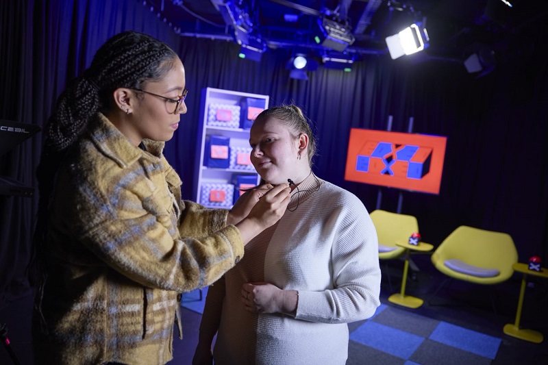 Adjusting a student's microphone on set in UON's TV studio