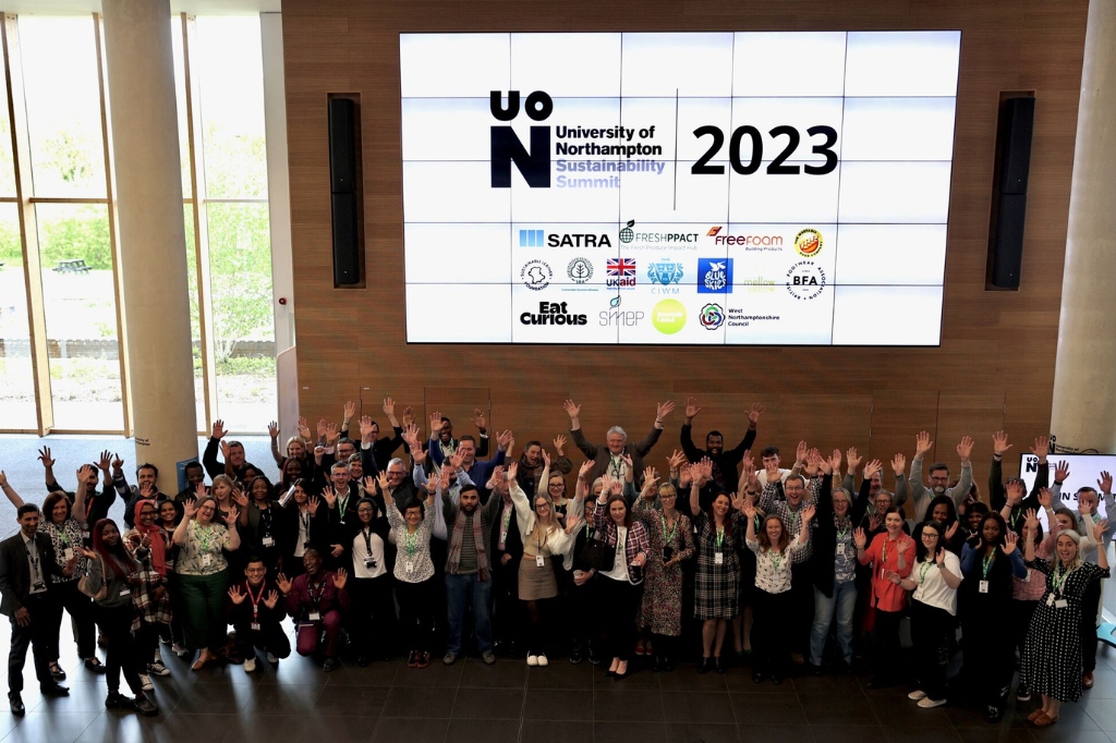 Group of people wave at camera in front of large screen