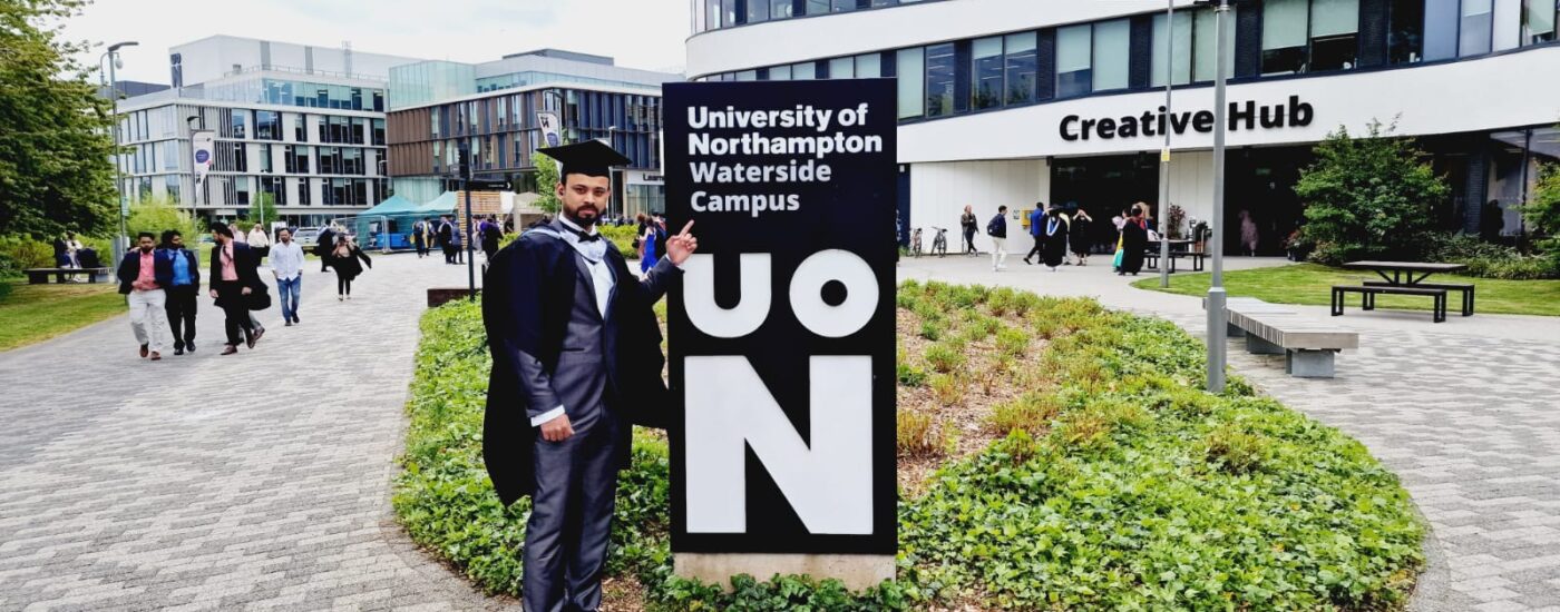Graduate Anas Mudassar wearing his graduation gown and mortarboard in front of the Creative Hub on campus during graduation day