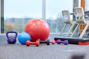 Four different coloured dumbbells in different sizes (red, black, pink and purple), a purple kettlebell, and two different sized exercise balls, next to a step in the Physiotherapy Laboratory.