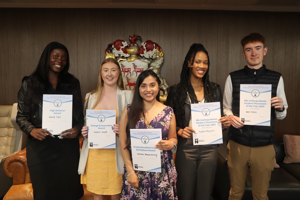 Five students stand in a group holding up certificates.