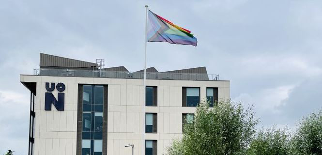 Pride flag outside of Senate Building, at the University of Northampton. The flag is high up and blowing in the wind. The sky is cloudy.