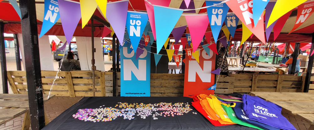 Stall at Northampton Pride, which has colourful bright bags and pronoun badge on offer, all in bright Pride related colours.