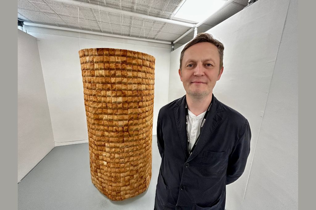 Dr Craig Staff stand with with a tower, approximately 2 meters high which is made of household teabags.
