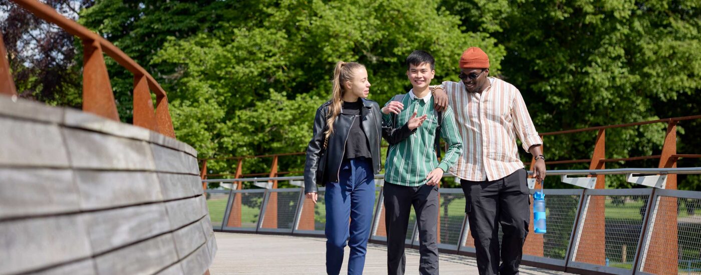 Three students cross the bridge from town into the University of Northampton campus