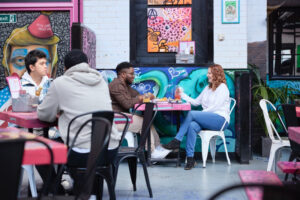 Two students sitting at a pink table, on white chairs, with bright graffiti style designs at a restaurant in Northampton.