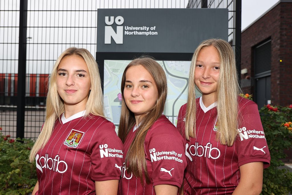 Three members of the NTFC Women's Team stand proudly displaying the University of Northampton logo.