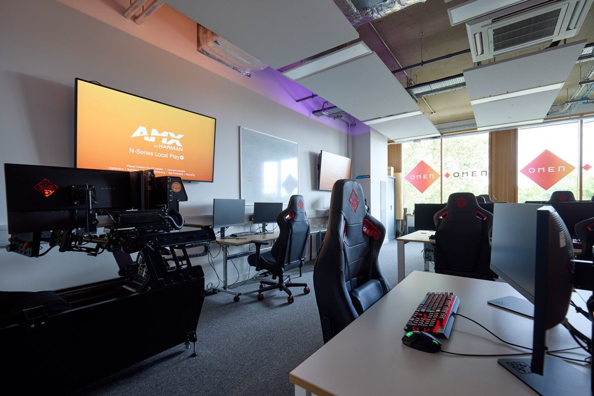 Internal view of the Computing and Games suite, where big screens are on the walls with game stations consisting of two screens, light up keyboard and mouse, and game chair, are dotted around the rom. There is branding of 'Omen' on the windows
