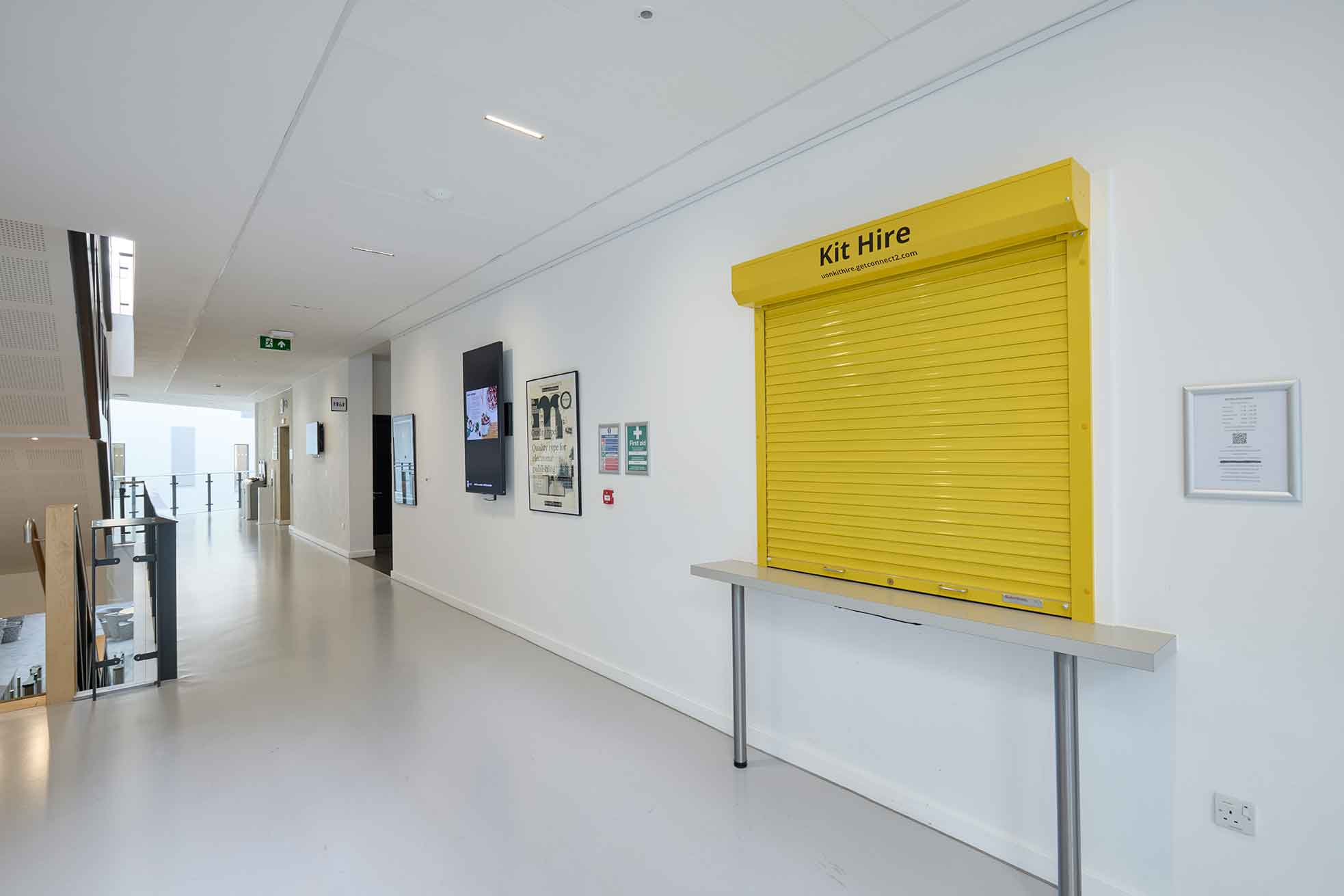 The photograph shows the yellow Kit Hire window with yellow shutters pulled down on the first floor corridor of the Creative Hub