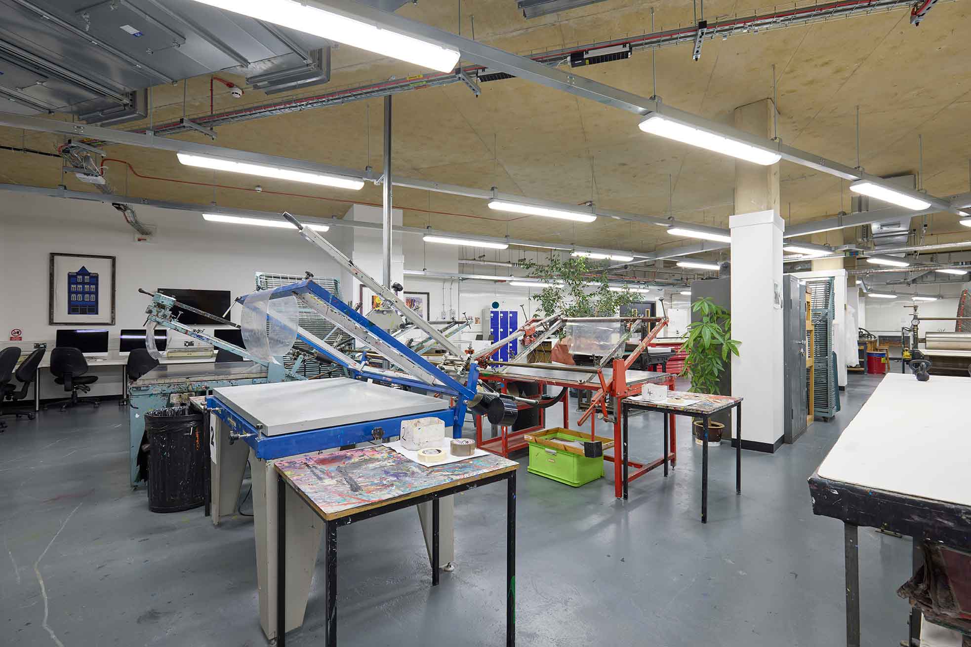 The photo shows the printmaking workshop at the University of Northampton. In the foreground are blue and white print presses and in the background is a variety of print-making equipment