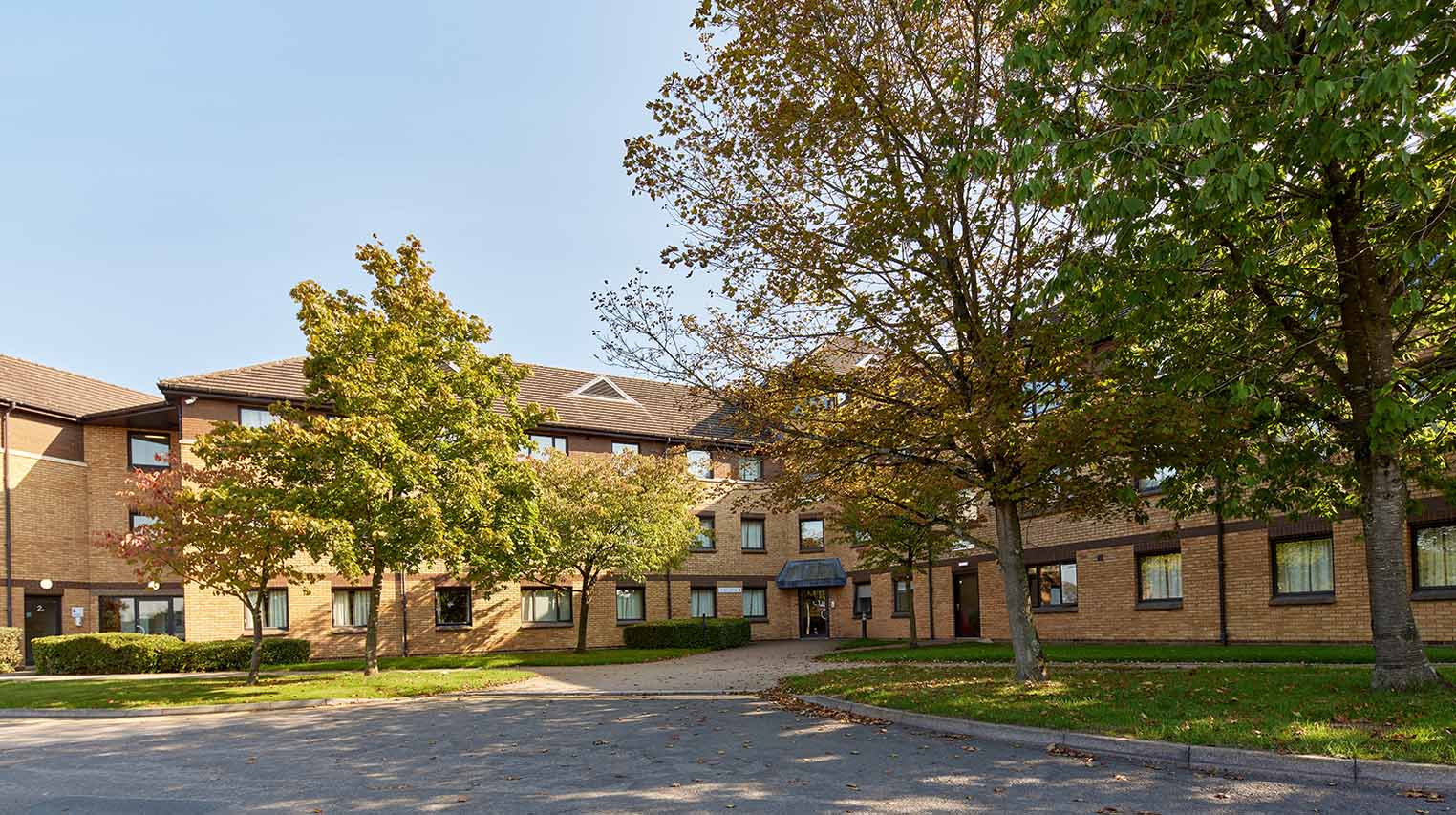 A picture of Scholars Green showing three-storey halls of residence built in an l-shape with trees in the foreground