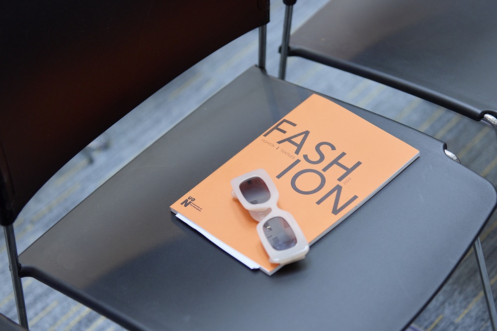 Pair of sunglasses resting on a UON Fashion show programme on a chair