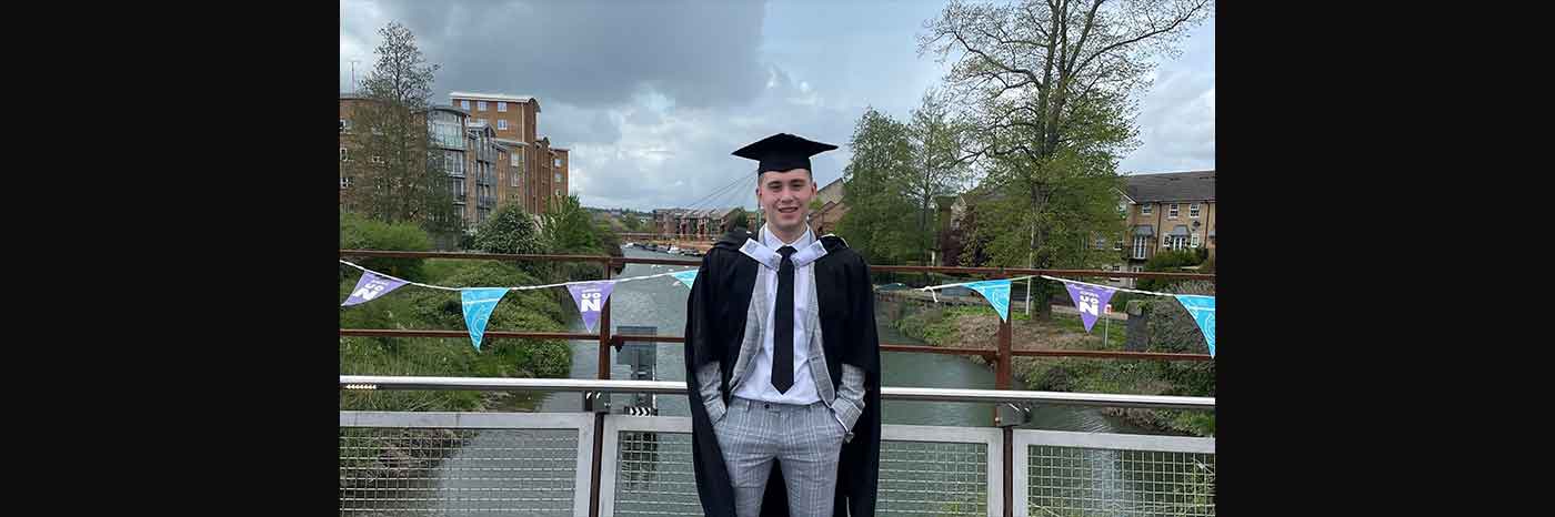 The photo shows Kieran Craddock who studied at the University of Northampton for a Strength and Conditioning MSc - Kieran is pictured wearing his graduation robes standing on a bridge with Northampton town in the background