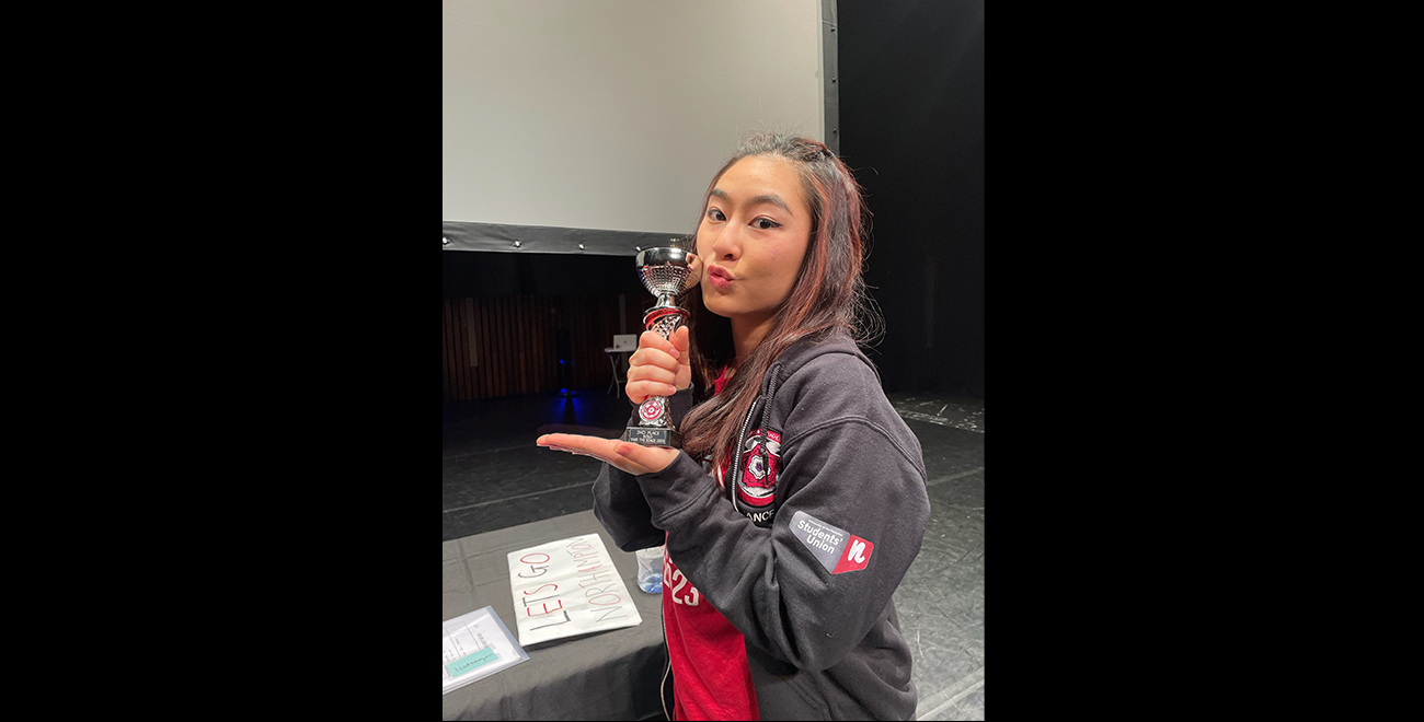 Emily Ng, a student, holding their trophy from their dance class and posing to the camera.
