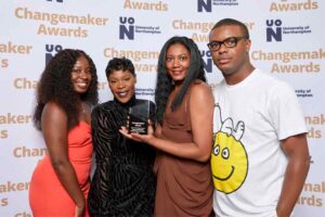 Four representatives from the Black Criminology Network pose for a photo in front of a photo backdrop at the 2023 UON Changemaker Awards. The representatives are holding the award for Culture, Heritage and Environment Changemaker of the Year