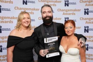Three representatives from The Factory Hair Studio pose for a photo in front of a photo backdrop at the 2023 UON Changemaker Awards. The representatives are holding the award for Runner-Up the Changemaker People’s Choice Award