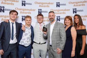 Six members of the team from The Frank Bruno Foundation pose for a photo in front of a photo backdrop at the 2023 UON Changemaker Awards. The team are holding their award for Health and Wellbeing Changemaker of the Year
