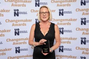 Jenny Munro poses for a photo in front of a photo backdrop at the 2023 UON Changemaker Awards. Jenny holds her award for Student Changemaker of the Year
