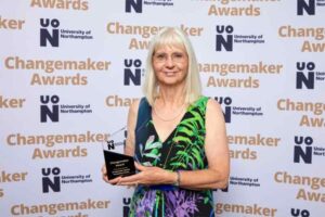 Linda Davis-Sinclair poses for a photo in front of a photo backdrop at the 2023 UON Changemaker Awards. Linda holds her Changemaker Special Recognition Award