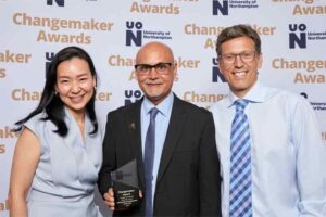 Three representatives from the Village International Education Centre pose for a photo in front of a photo backdrop at the 2023 UON Changemaker Awards. The representatives are holding the award for International Changemaker of the Year