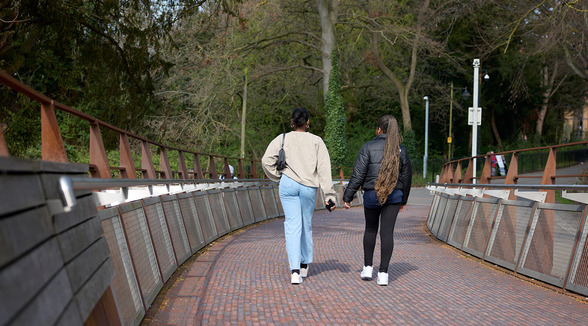 Two students walking away from the camera, across the bridge.
