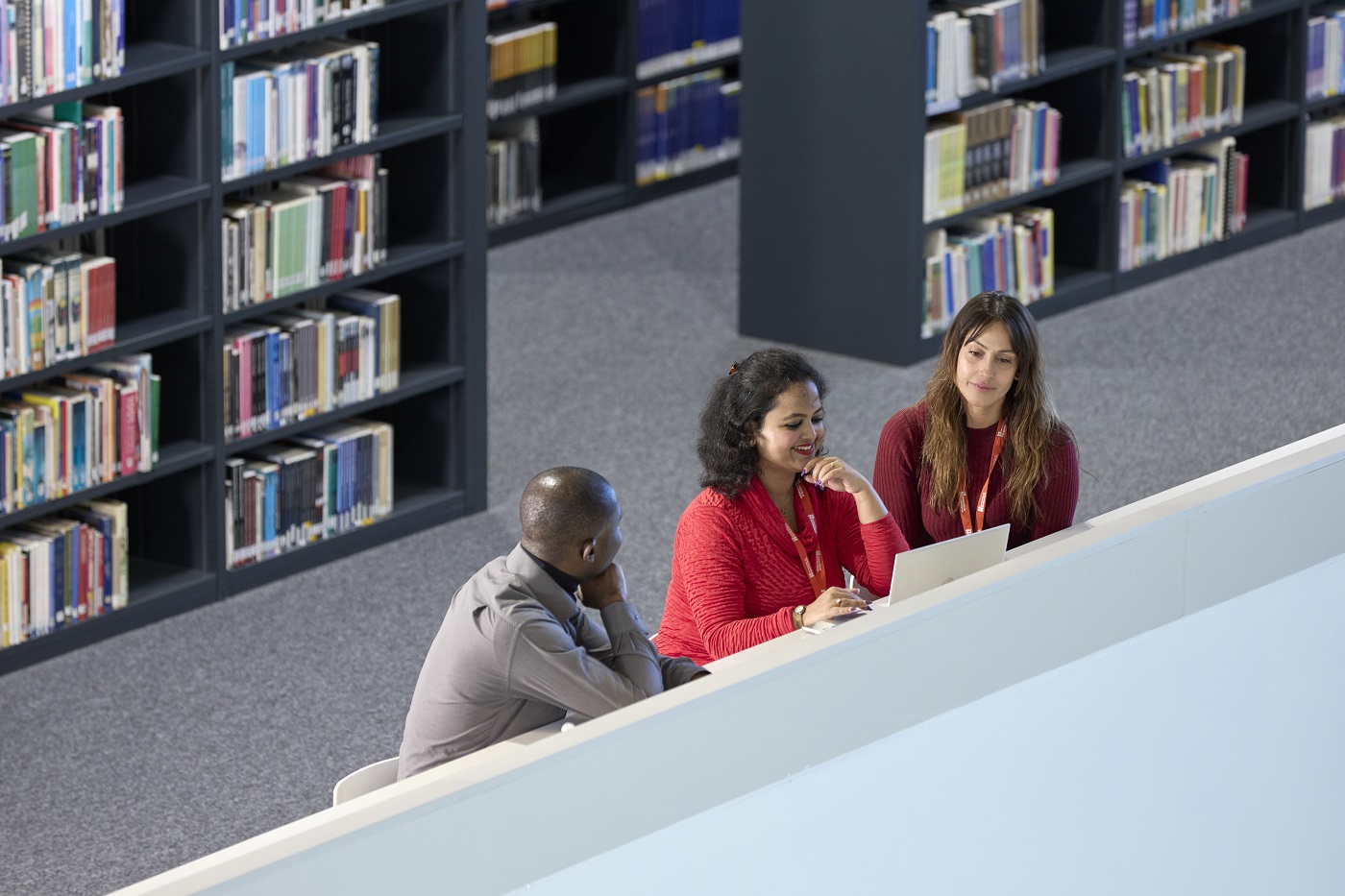 Three mature students sit in front of a laptop in a library