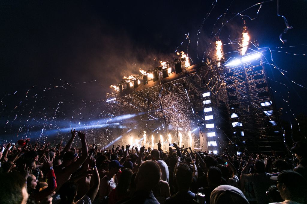 Thousands of concerts goers in front of a stage full of lights, fireworks and streamers.