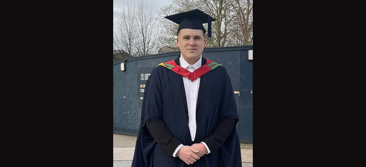 Deividas Misiunas in graduation robes standing in front of a building.