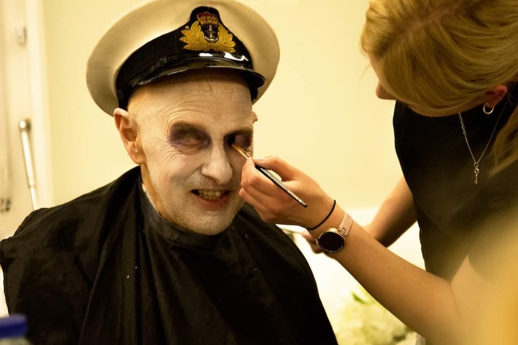 Student applies make-up to character's face.