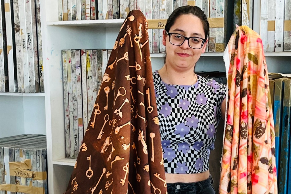 Student holds two fabrics up and smiles at camera.