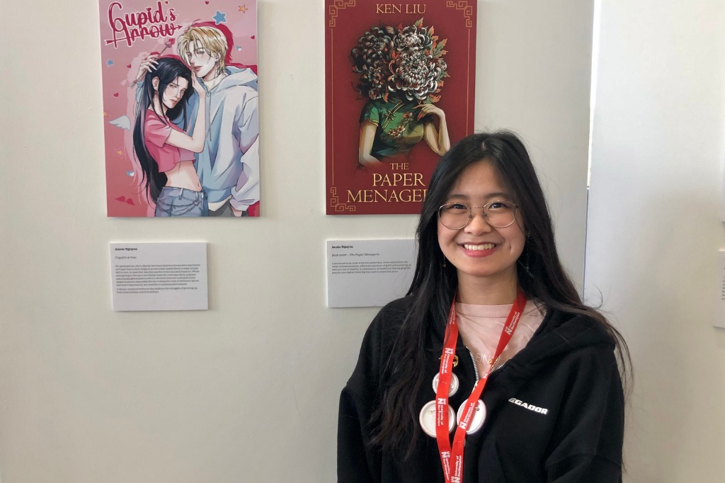 Student smiles at camera standing next to her Illustration designs.