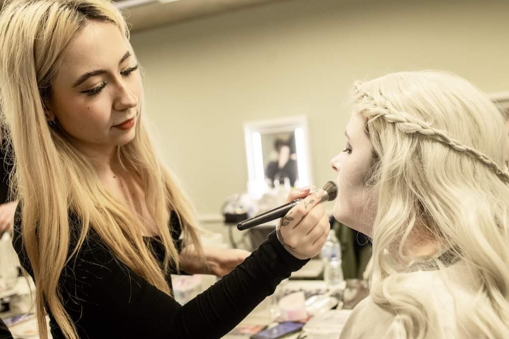 Student applies makeup to actor using brush.
