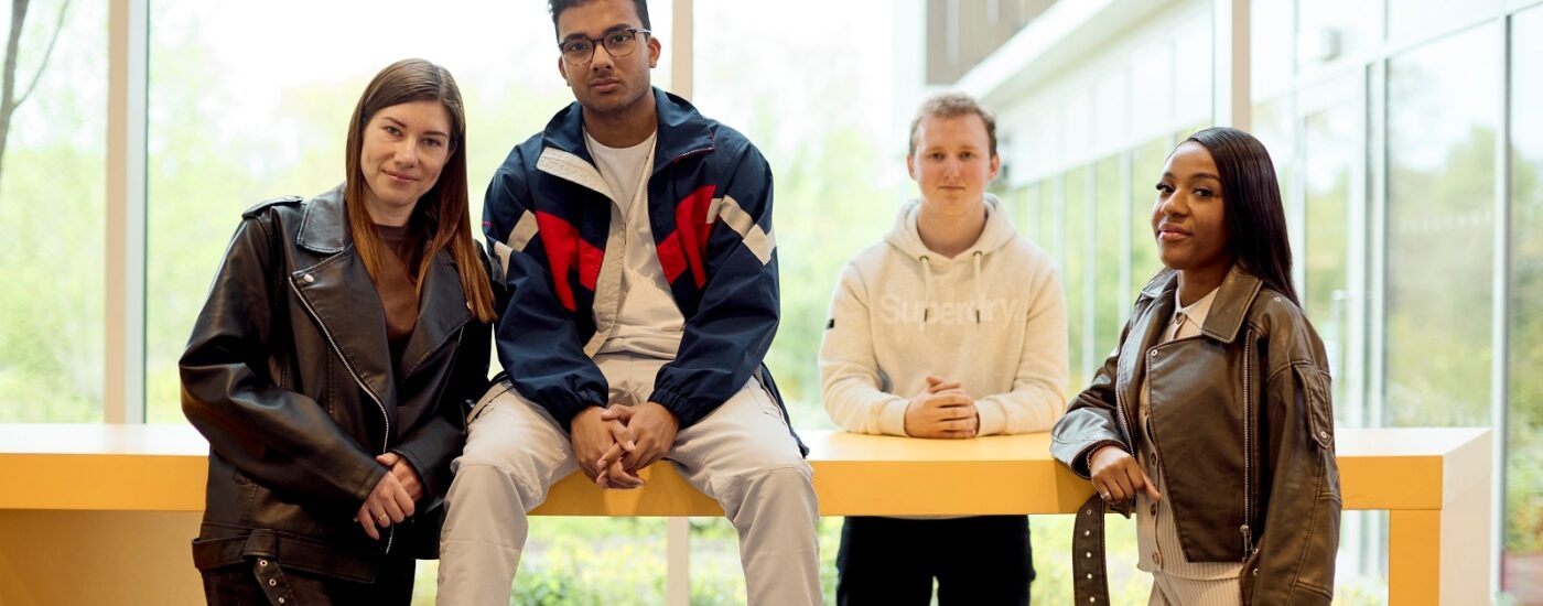 Four UON students stand and sit casually around a yellow table in the bright Learning Hub with large windows.